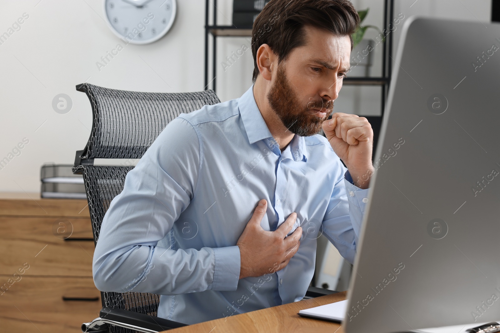 Photo of Sick man coughing at workplace in office. Cold symptoms