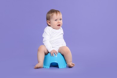 Photo of Little child sitting on baby potty against violet background