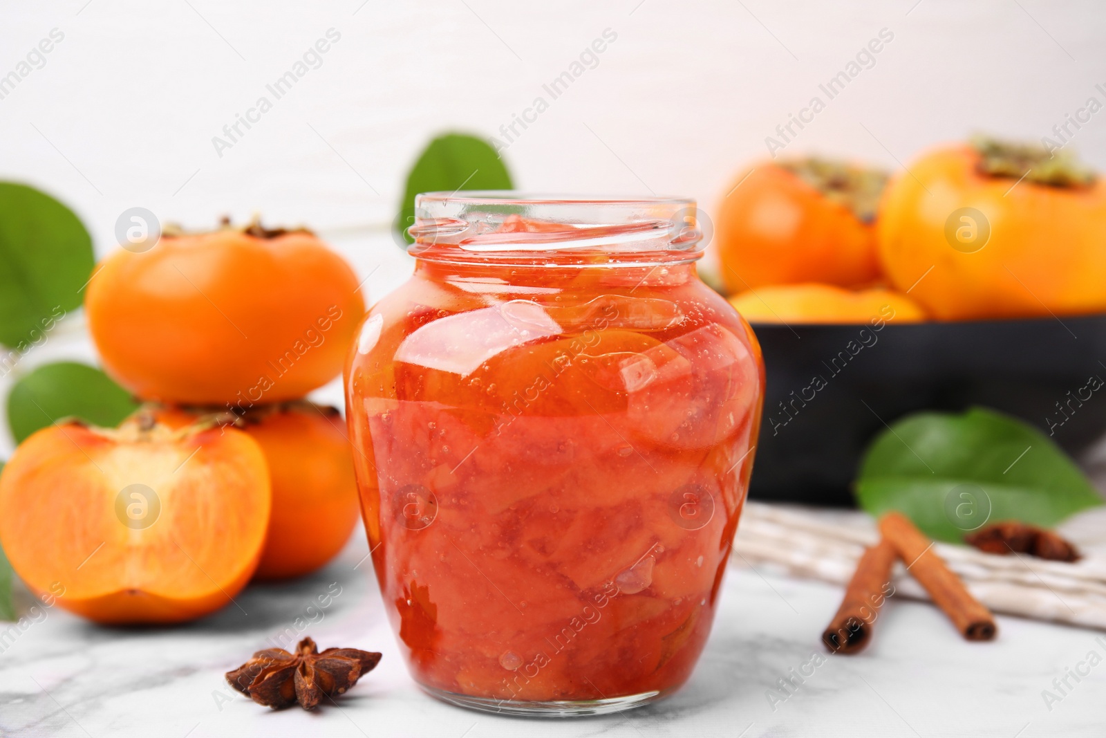 Photo of Jar of tasty persimmon jam and ingredients on white marble table