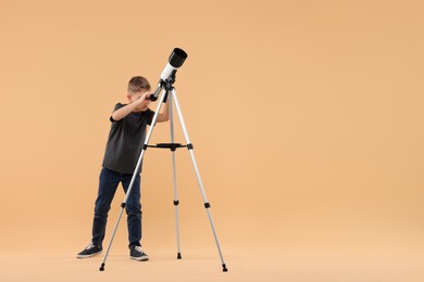 Little boy looking at stars through telescope on beige background, space for text