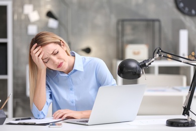 Photo of Young woman suffering from headache in office