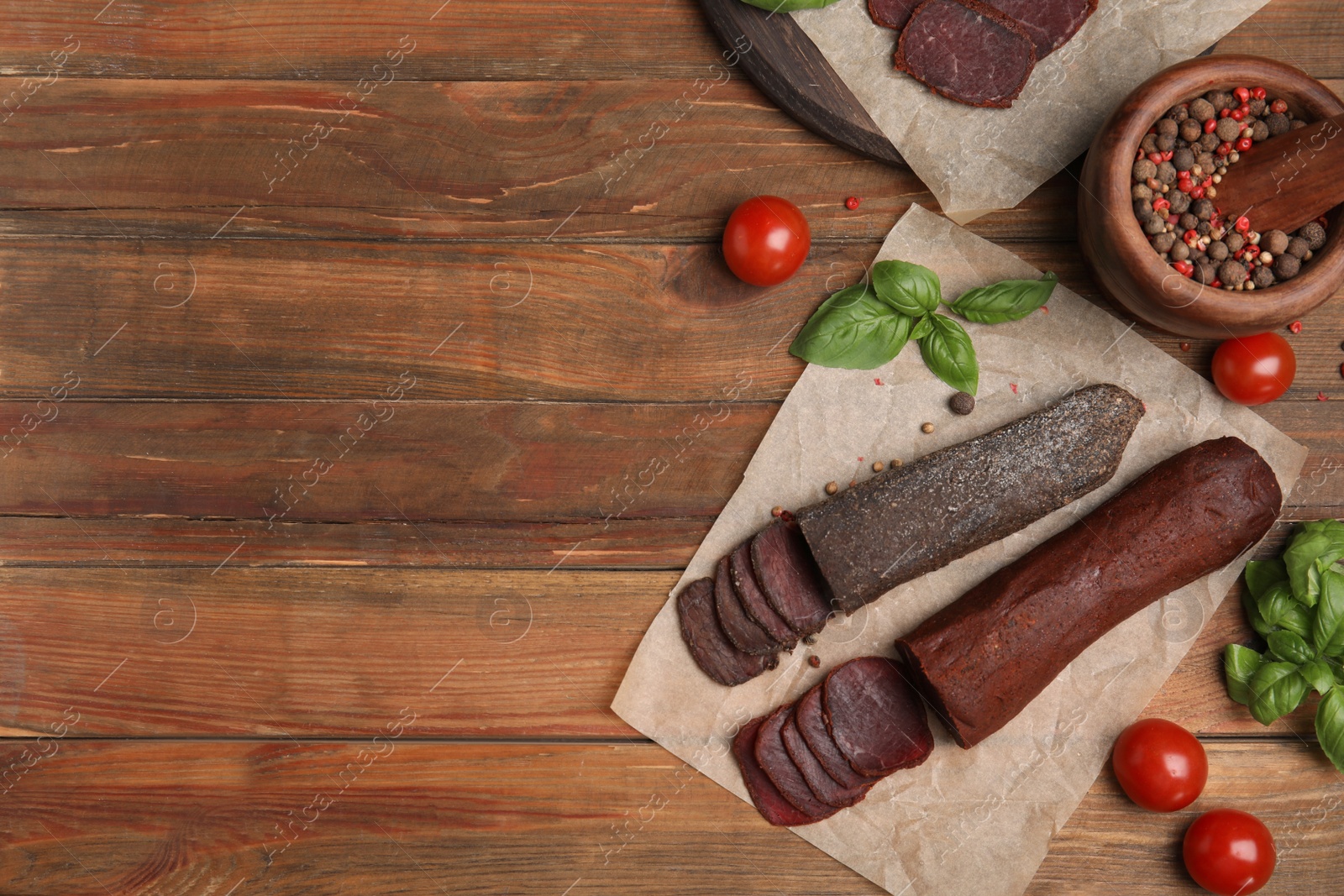 Photo of Delicious dry-cured beef basturma with basil and tomatoes on wooden table, flat lay. Space for text