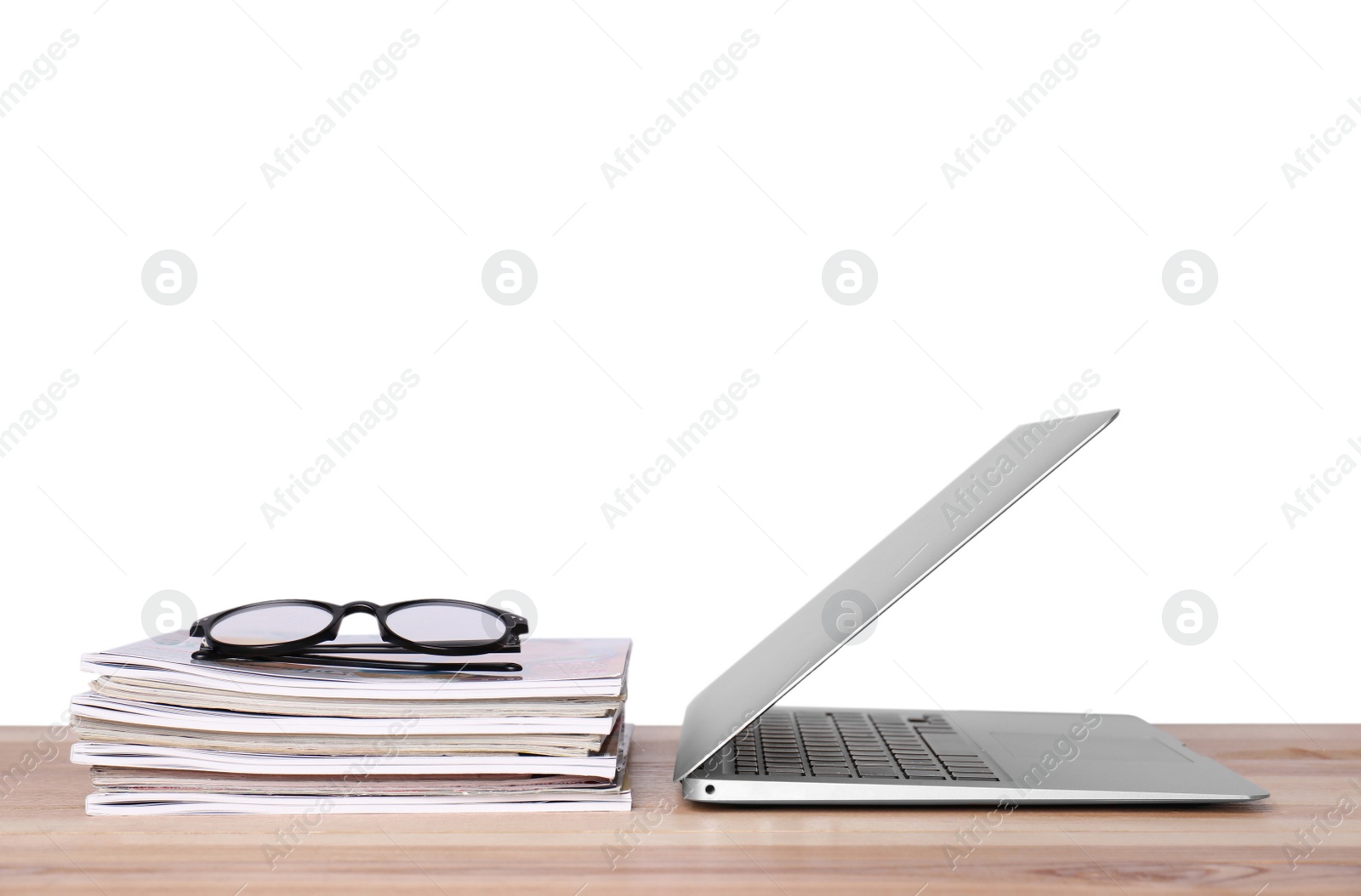 Photo of Laptop, glasses and stack of magazines on wooden table