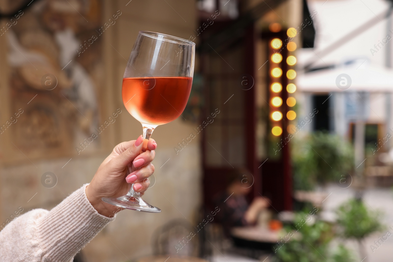 Photo of Woman holding glass of rose wine outdoors, closeup. Space for text