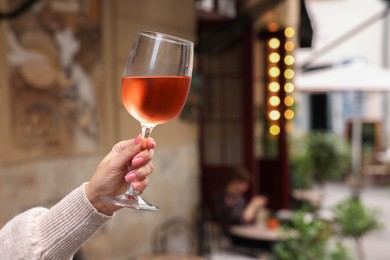 Woman holding glass of rose wine outdoors, closeup. Space for text