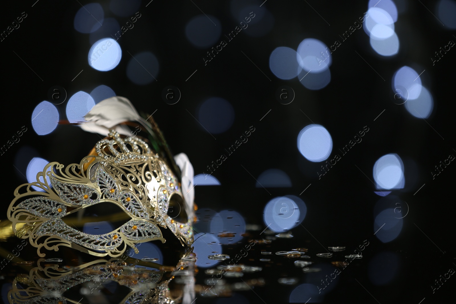 Photo of Beautiful carnival mask on table against blurred lights. Space for text