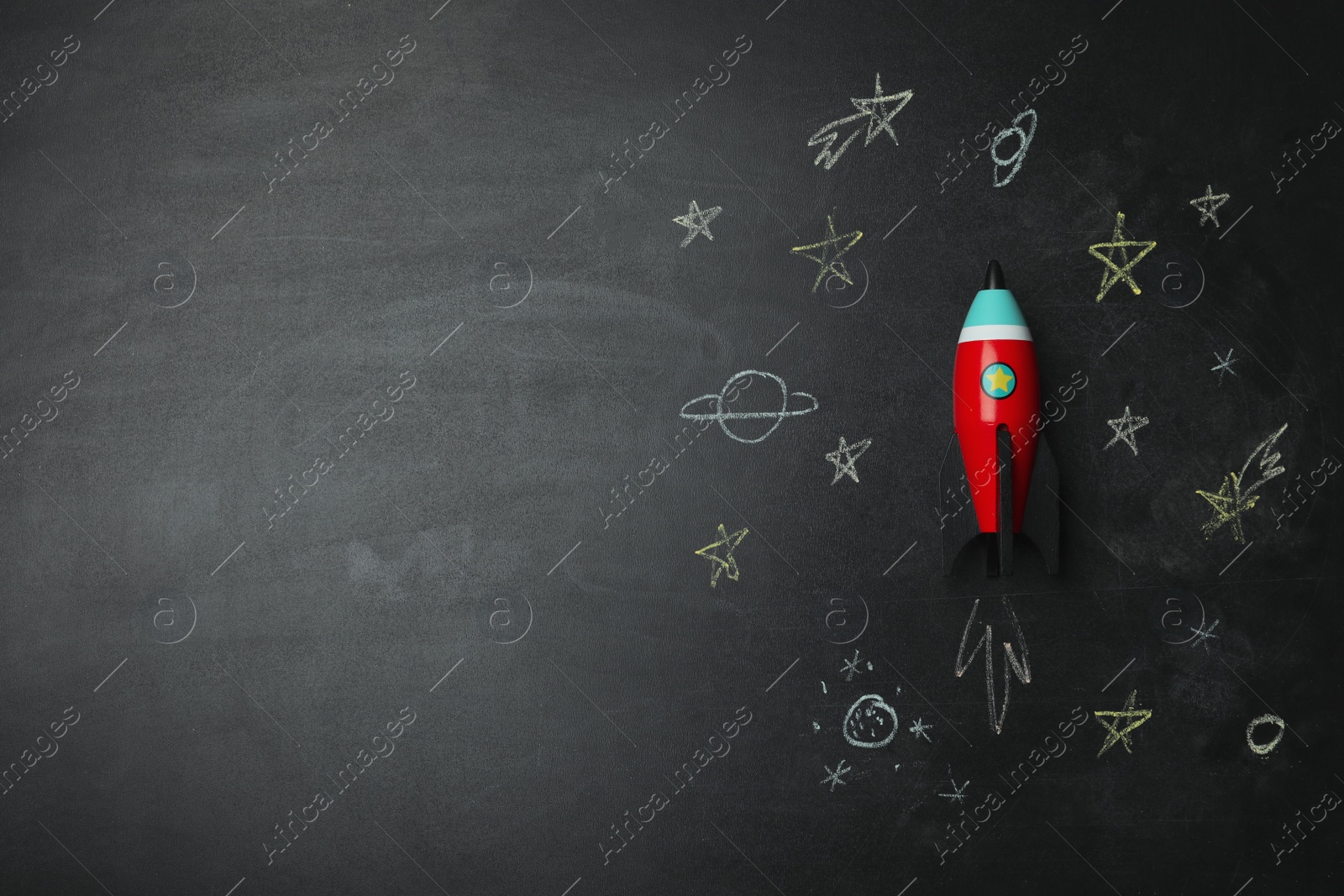 Photo of Bright toy rocket and drawings on chalkboard, flat lay. Space for text