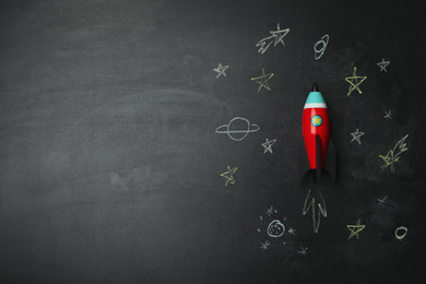 Photo of Bright toy rocket and drawings on chalkboard, flat lay. Space for text