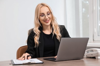 Happy secretary working with laptop at table in office