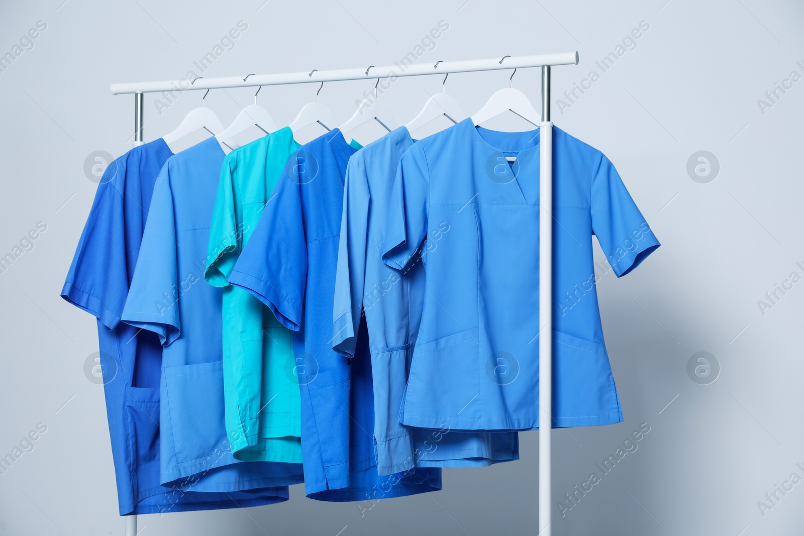 Photo of Different medical uniforms on rack against light grey background