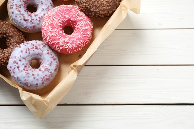 Photo of Delicious glazed donuts on white wooden table, top view. Space for text