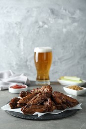 Photo of Delicious chicken wings served with glass of beer on grey table, space for text