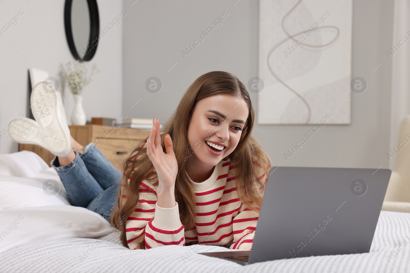 Photo of Happy woman having video chat via laptop on bed in bedroom