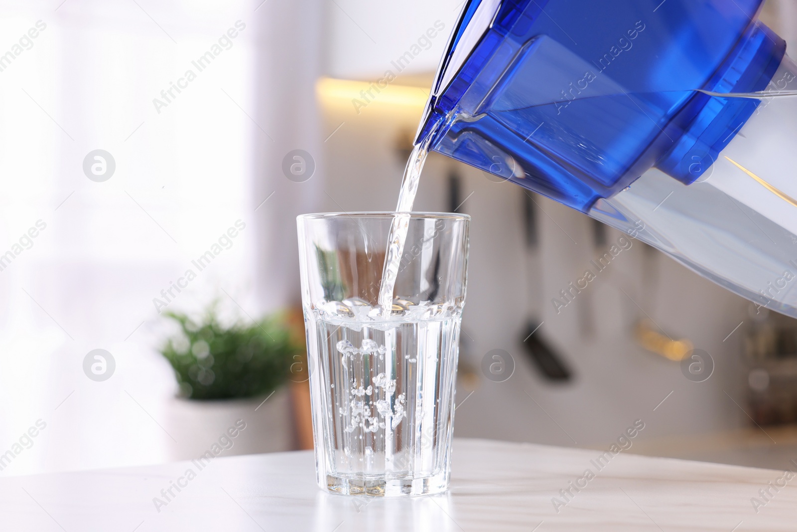 Photo of Pouring water from filter jug into glass in kitchen, closeup