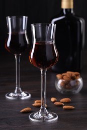 Photo of Liqueur glasses with tasty amaretto and almonds on wooden table, closeup