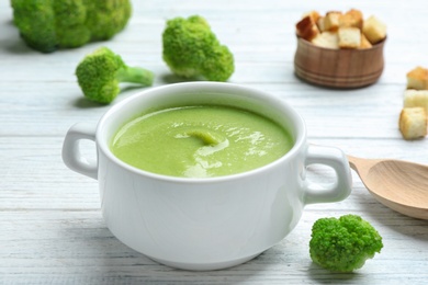 Photo of Bowl of broccoli cream soup served on white wooden table