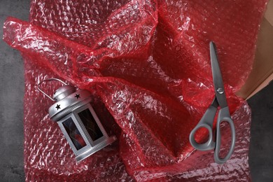 Beautiful decorative lantern, red bubble wrap, scissors and cardboard box on dark grey table, flat lay