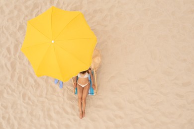 Image of Woman resting in sunbed under yellow beach umbrella at sandy coast, aerial view. Space for text