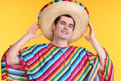 Photo of Young man in Mexican sombrero hat and poncho on yellow background