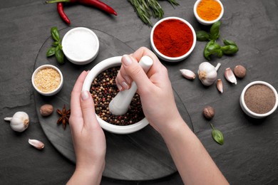 Photo of Woman grinding peppercorns in mortar at black table, top view