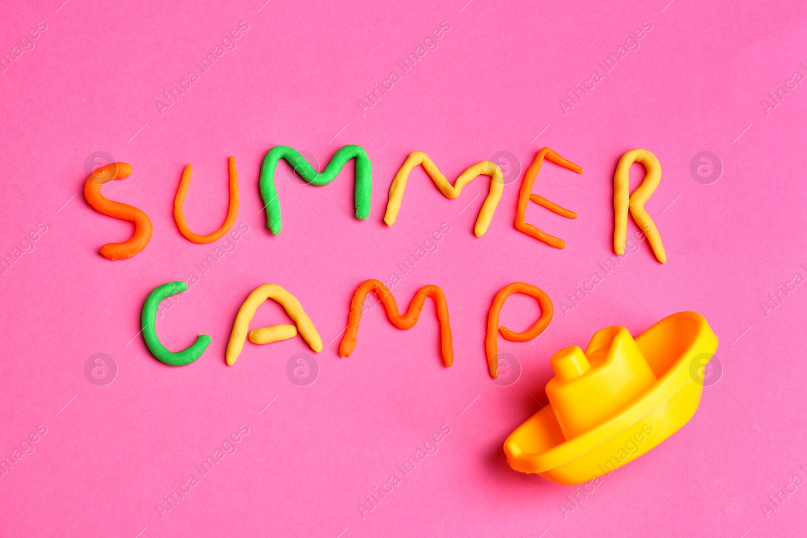 Photo of Words SUMMER CAMP made from modelling clay and plastic boat on color background, top view