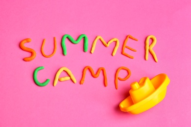 Photo of Words SUMMER CAMP made from modelling clay and plastic boat on color background, top view