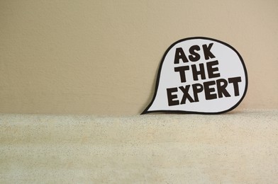 Photo of Paper message bubble with phrase Ask The Expert near beige wall, space for text