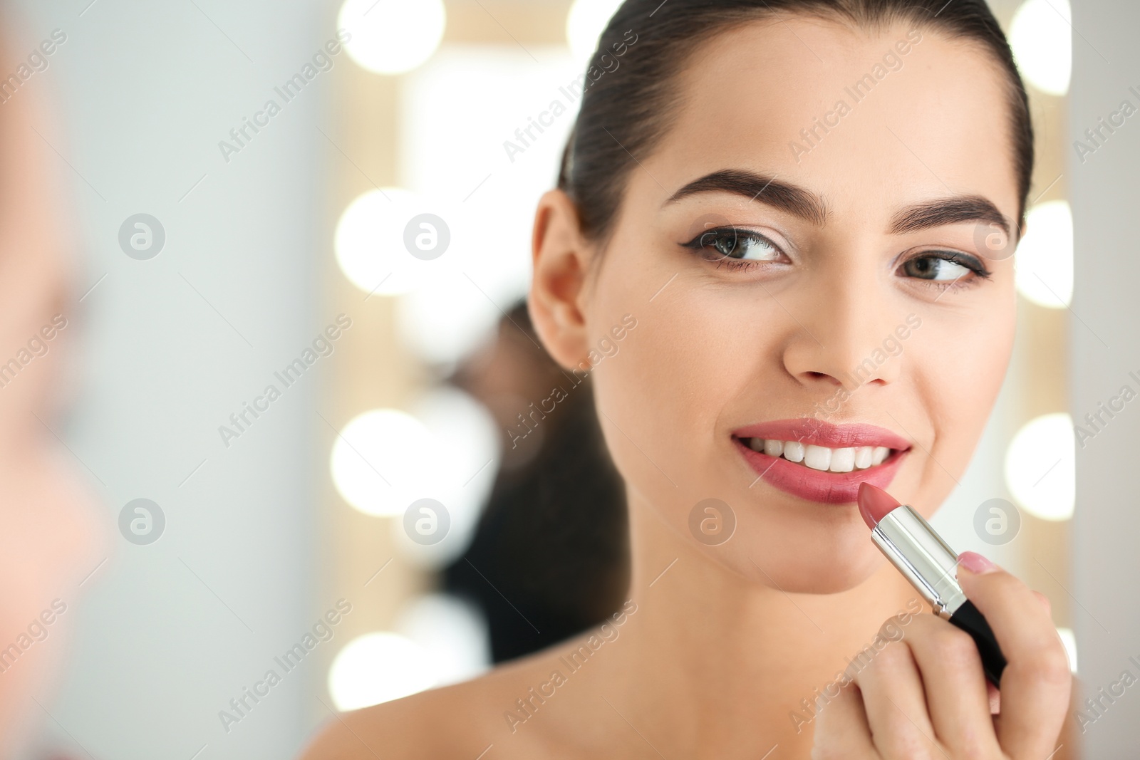 Photo of Young woman applying lipstick in front of mirror