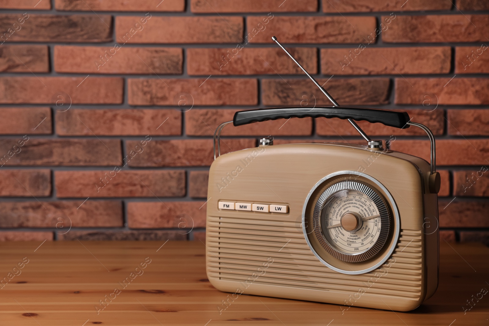 Photo of Retro radio receiver on wooden table near red brick wall. Space for text