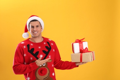 Photo of Handsome man in Santa hat holding gift boxes on yellow background