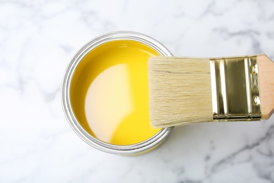 Photo of Can with yellow paint and brush on marble background, top view