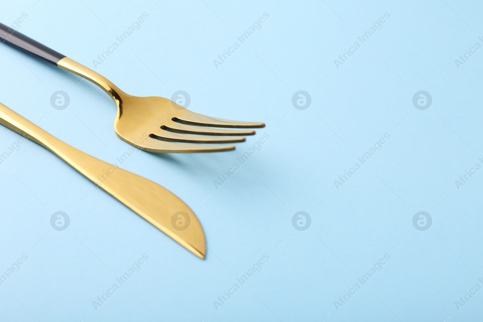 Photo of Stylish cutlery. Golden knife and fork on light blue background, closeup. Space for text