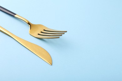 Stylish cutlery. Golden knife and fork on light blue background, closeup. Space for text