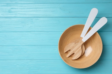 Fork and spatula in wooden bowl on light blue table, flat lay with space for text. Cooking utensils