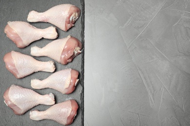 Photo of Slate plate with raw chicken drumsticks and space for text on gray background, top view. Fresh meat