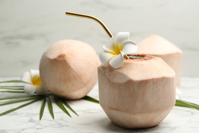 Photo of Young peeled coconut with straw and flowers on white marble table. Space for text