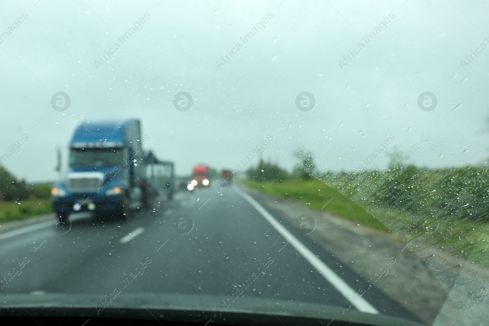 Photo of Blurred view of country road through wet car window. Rainy weather