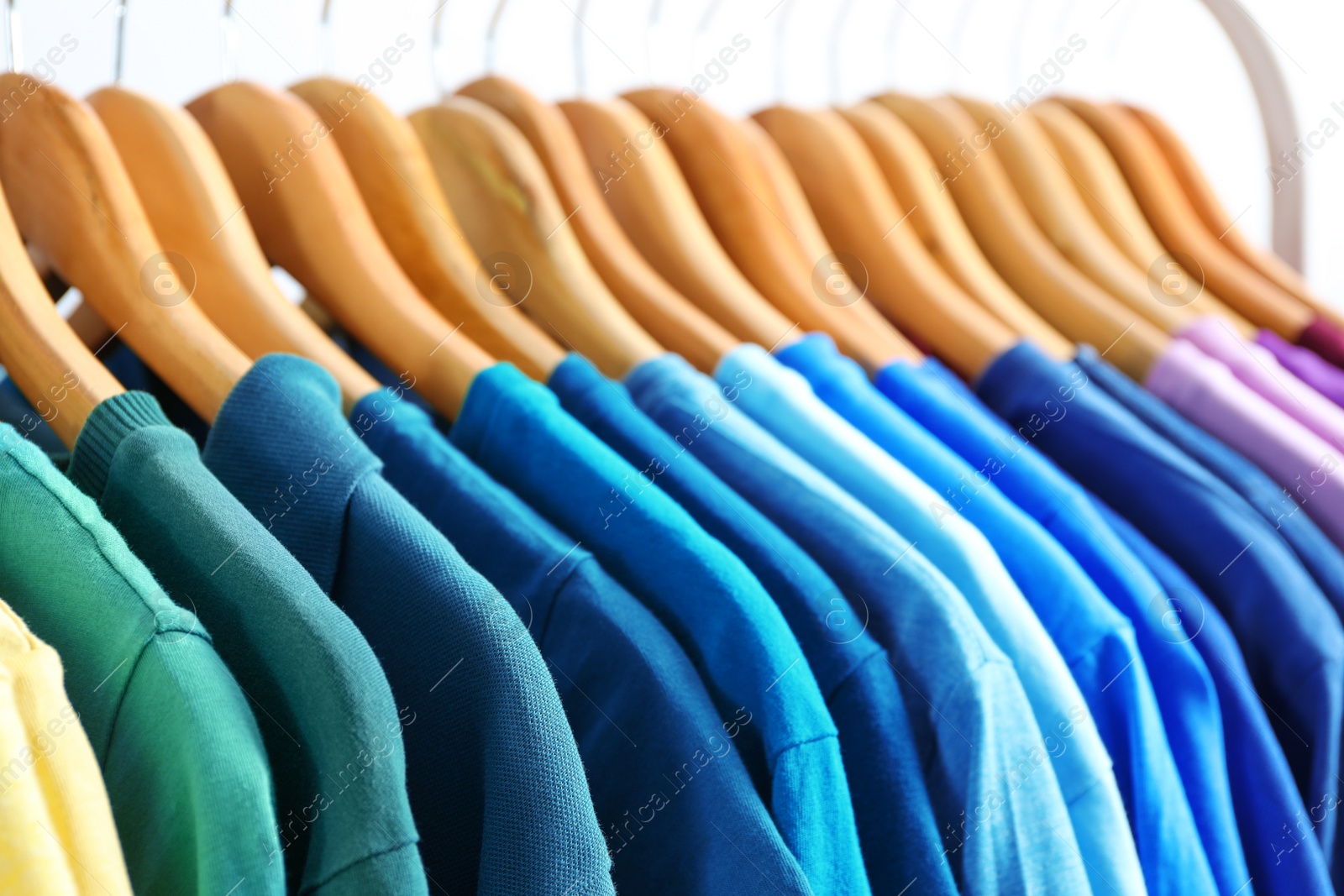 Photo of Hangers with bright clothes on light background, closeup