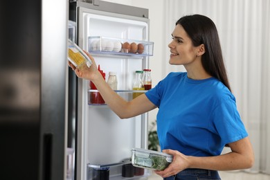 Young woman taking containers with vegetables out of refrigerator indoors