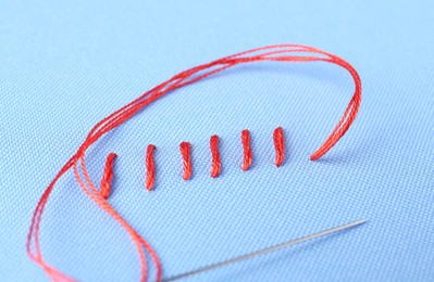 Photo of Sewing needle with thread and stitches on light blue cloth, closeup