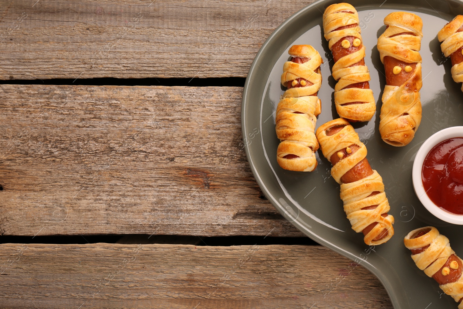 Photo of Cute sausage mummies served with ketchup on wooden table, top view with space for text. Halloween party food