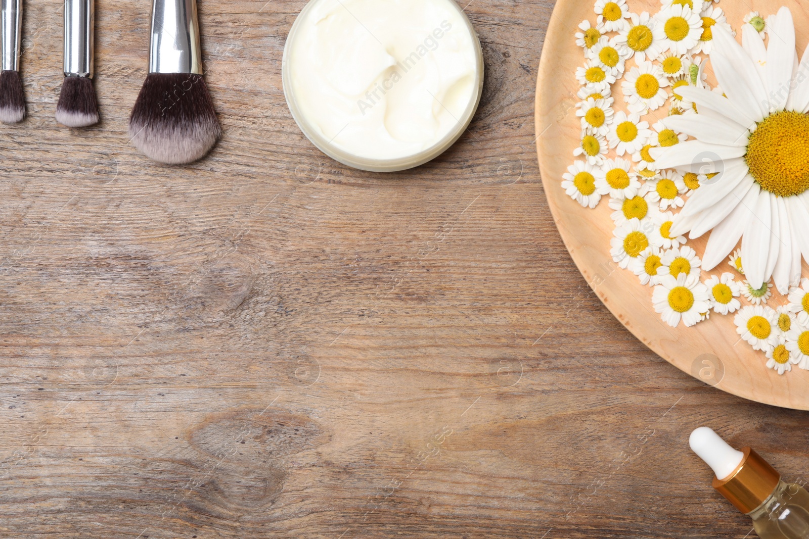 Photo of Flat lay composition with chamomile flowers and cosmetic products on wooden table, space for text