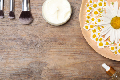 Photo of Flat lay composition with chamomile flowers and cosmetic products on wooden table, space for text