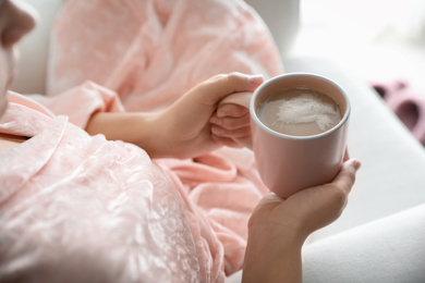 Woman with cup of hot drink at home in morning, closeup