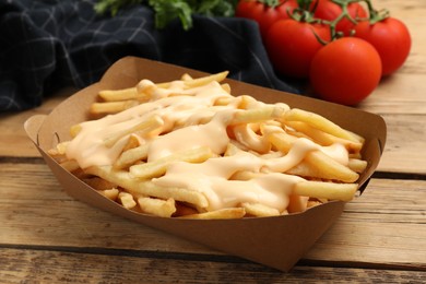 Delicious French fries with cheese sauce on wooden table, closeup