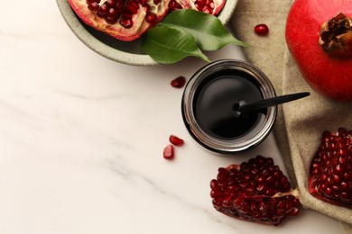 Photo of Glass jar of tasty pomegranate sauce and fresh ripe fruit on white marble table, flat lay. Space for text