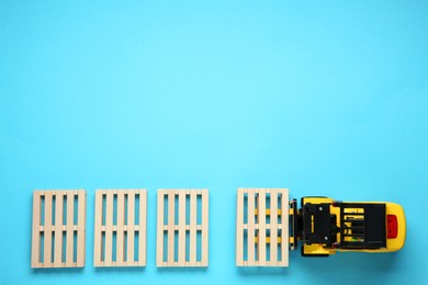 Toy forklift and wooden pallets on light blue background, flat lay. Space for text