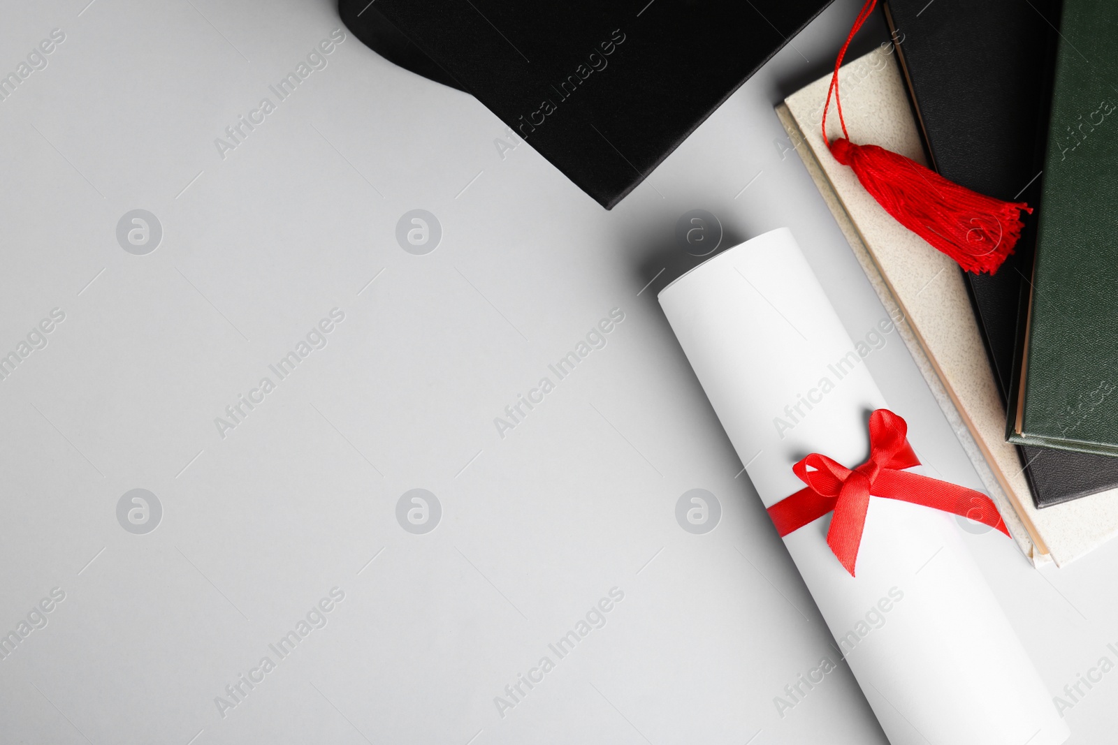 Photo of Graduation hat, books and student's diploma white background, top view. Space for text