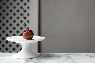 Photo of Sweet chocolate dipped cherry on white marble table, space for text