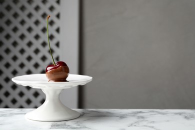 Sweet chocolate dipped cherry on white marble table, space for text